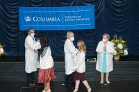 Two students giving elbow bumps to faculty members after donning their white coats